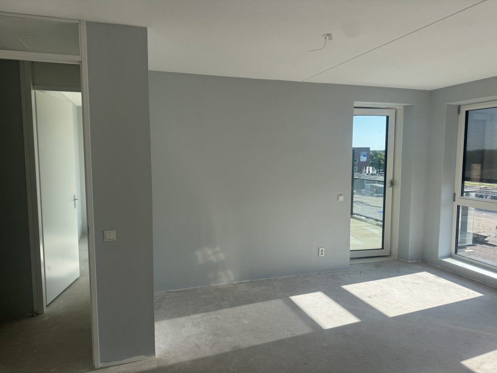 Nieuwbouwappartement met een betonvloer, een gesausde wand en een deur naar het balkon