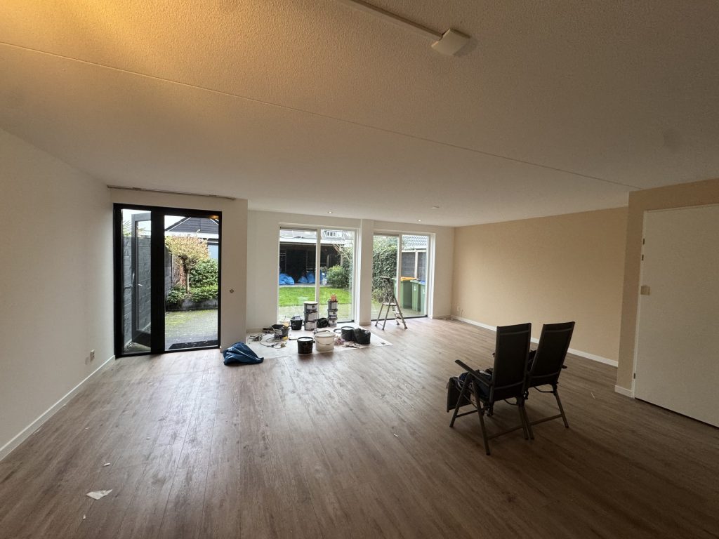 Ruime woonkamer met lichte wanden en tuindeuren, verfemmers staan klaar voor het sauswerk