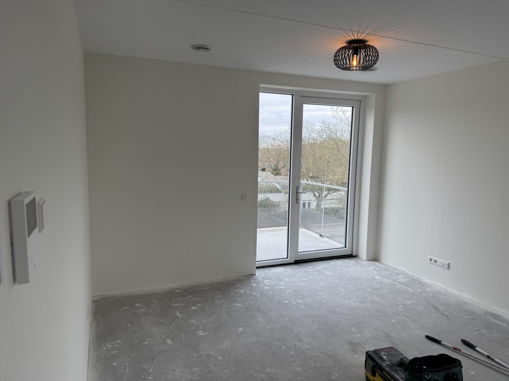 Kale appartementskamer met openslaande deuren naar een balkon, net na de oplevering