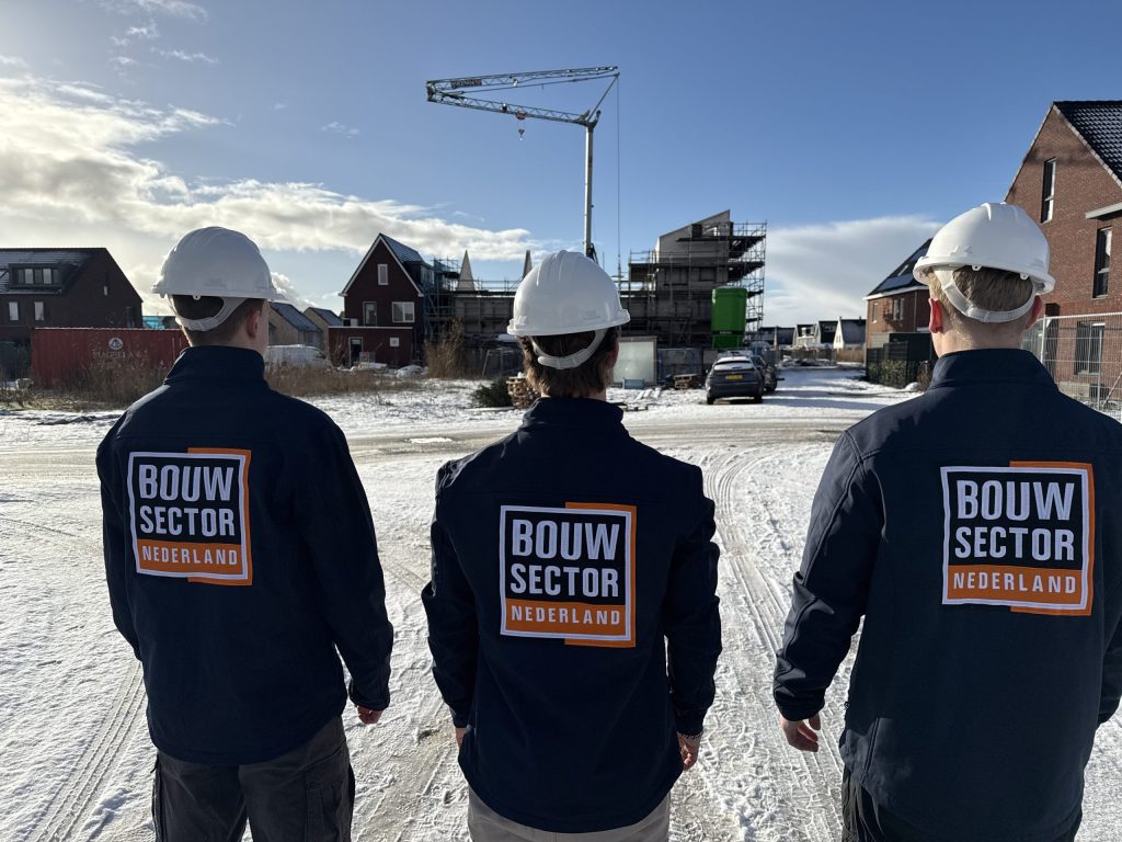 Drie vakmensen met witte helm voor een rij nieuwe woningen