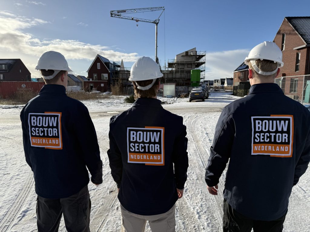 Drie vakmensen van Bouwsector Nederland met witte helm voor een straat met nieuwbouwhuizen in aanbouw